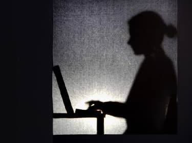 De foto toont een schaduw op de muur van een persoon achter de computer