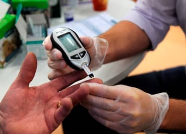 foto toont een diabetespatiënt waarbij met een bloedglucosemeter het bloed wordt gecontroleerd door middel van een vingerprik