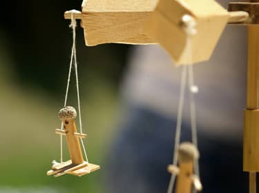 De foto toont een weegschaal van hout met twee houten poppetjes eraan