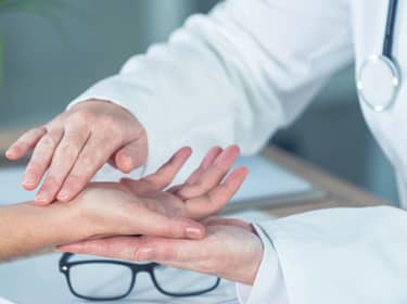 De foto toont een arts die de pols van een patiënt onderzoekt