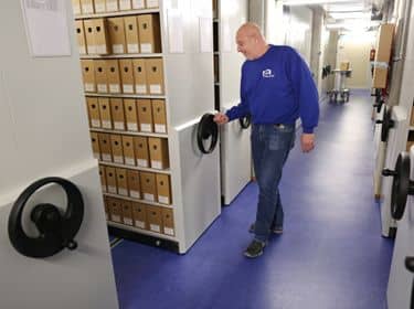 De foto toont een man bij een kast met archiefmappen