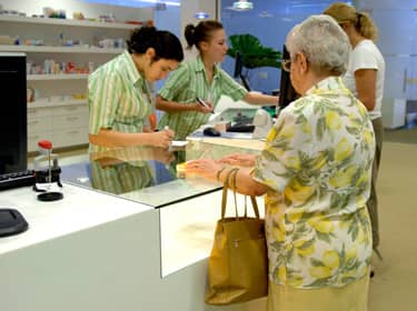 De foto toont een vrouw aan de balie van een apotheek