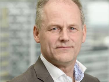 De foto toont Peter Siebers. Hij heeft kort grijs haar en draagt een grijs pak en een wit overhemd.