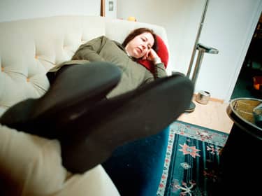 De foto toont een vrouw die vermoeid op de bank ligt