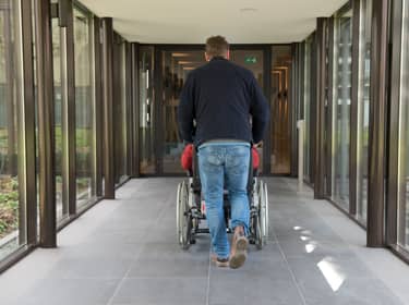 De foto toont een man die iemand in een rolstoel voortduwt