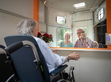 De foto toont een vrouw in een rolstoel aan de balie van een instelling