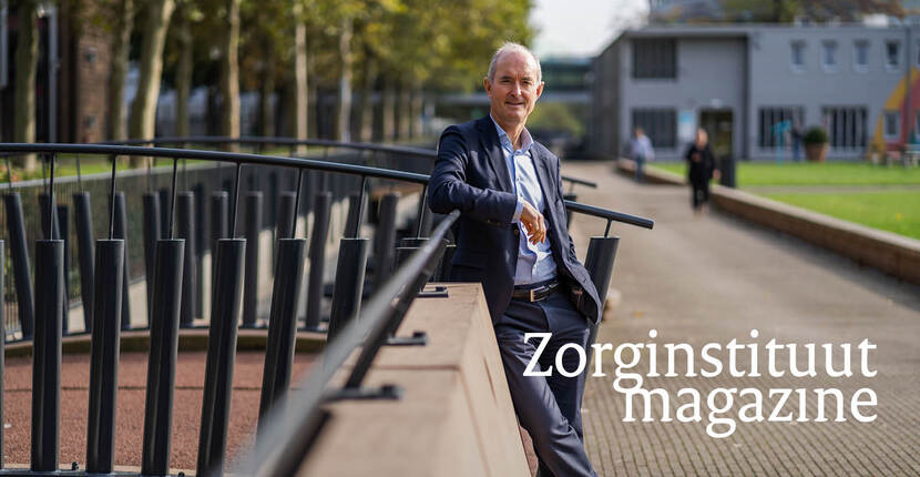 De foto toont Jan Kremer, een man met grijs haar in een donkerblauw pak. We zien hem ten voeten uit, hij leunt tegen de leuning van een brug, houdt zijn linkerarm op de leuning en heeft zijn rechterhand in zijn zak.