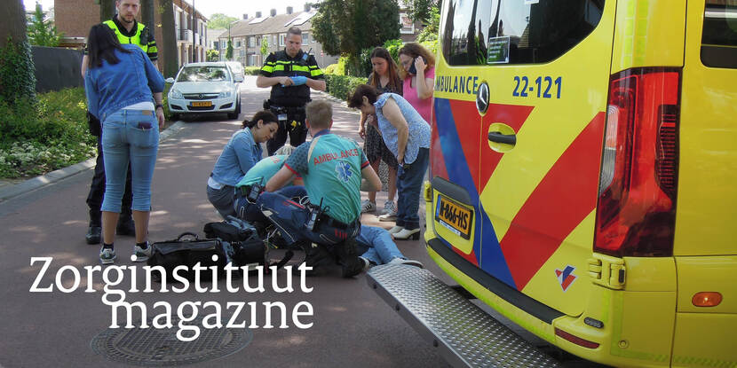 Op een autoweg staat een groep mensen waaronder ambulancepersoneel om een gewond persoon heen en een ambulance