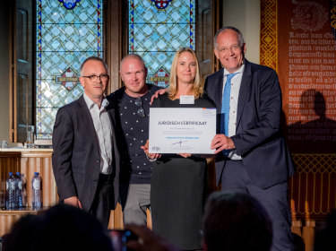 De foto laat de overhandiging zien van het eerste juridische certificaat voor een blockchain oplossing in de zorg aan Erik Gerritsen