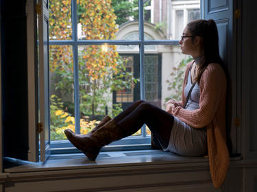 De foto toont een tienermeisje dat op de vensterbank zit en uit het raam kijkt