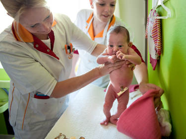 De foto toont een kraamverzorgster die een baby vasthoudt