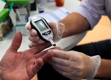 foto toont een diabetespatiënt waarbij met een bloedglucosemeter het bloed wordt gecontroleerd door middel van een vingerprik