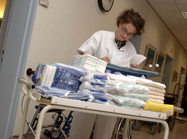 De foto toont een verpleegster met een kar vol met hulpmiddelen