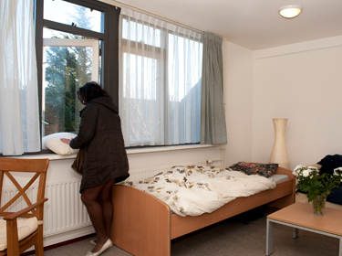 De foto toont een vrouw die haar beddengoed uithangt over het geopende raam van haar kamer in de GGZ instelling