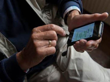 De foto toont een smartphone die wordt vastgehouden door een ouder persoon