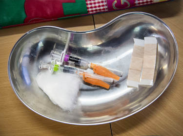 De foto toont een tafel met een dienblad met daarop twee spuiten, watjes en pleisters