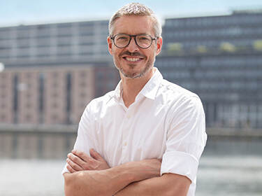 Op de afbeelding staat Sjoerd Repping aan een kade, op de achtergrond zien we water en gebouwen. Hij heeft kort grijs haar en een stoppelbaard. Hij draagt een zwarte bril en een wit overhemd. Repping staat met zijn armen over elkaar en kijkt lachend de camera in.