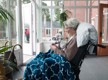 De foto toont een oudere vrouw in de hal van een verpleegtehuis