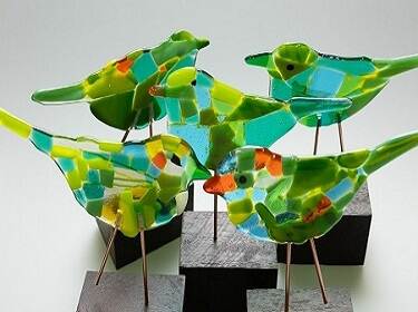 De foto toont beeldjes van Groene Vink 2019. Het zijn vijf identieke beeldjes van groene vogeltjes, gemaakt van staal en gekleurd glas.
