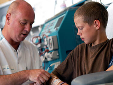 De afbeelding toont een jongen die door een arts aan een dialysemachine wordt aangesloten