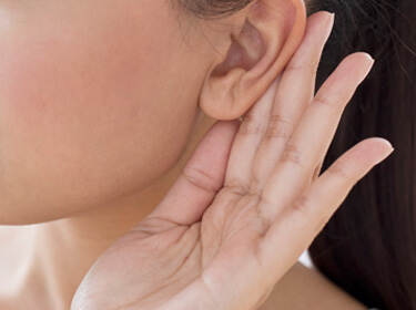 De foto toont een hand die achter een oor wordt gehouden om geluid te versterken