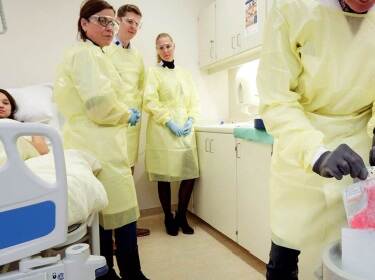 De foto toont vier zorgverleners in gele beschermende kleding, die een behandeling voorbereiden voor een patiënt