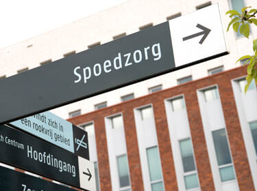 De foto toont een verwijsbord bij een ziekenhuis voor de ingang van de spoedzorg