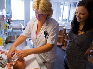 De foto toont een verpleegster die kijkt of een baby gezond is en de moeder die erbij staat