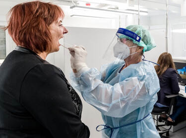 De foto toont een zorgmedewerker die in beschermende kleding een coronatest bij iemand afneemt
