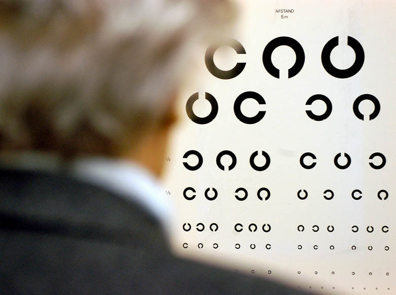 De foto toont iemand die een oogtest doet door naar een logMARkaart te kijken, een kaart met rijen letters die steeds kleiner worden.