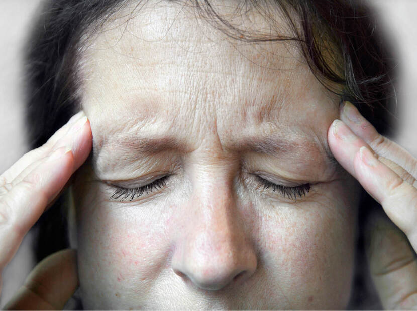 De foto toont een vrouw die met een pijnlijke frons haar vingers tegen de slapen drukt.
