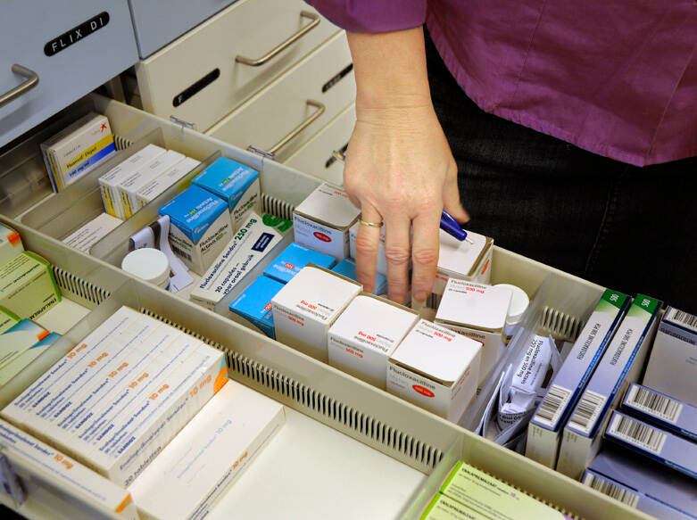 Op de foto staat een geopende la vol met verschillende doosjes medicijnen. Een hand, waarschijnlijk van een apotheker, pakt een doosje.