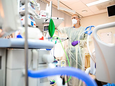 De foto toont een arts met mondkapje in een kamer met veel medische apparatuur