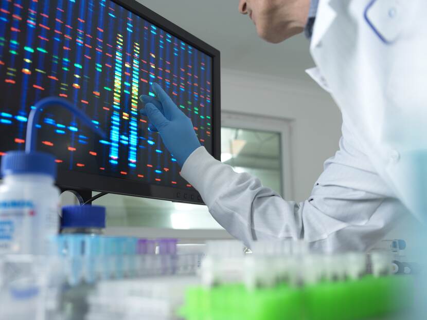 De foto toont een laboratorium. Op de voorgrond kijkt een medewerker op een computerscherm.